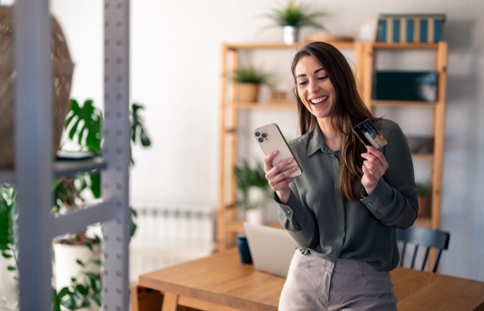 elinde telefon ve banka kartı tutan gülümseyen kişi