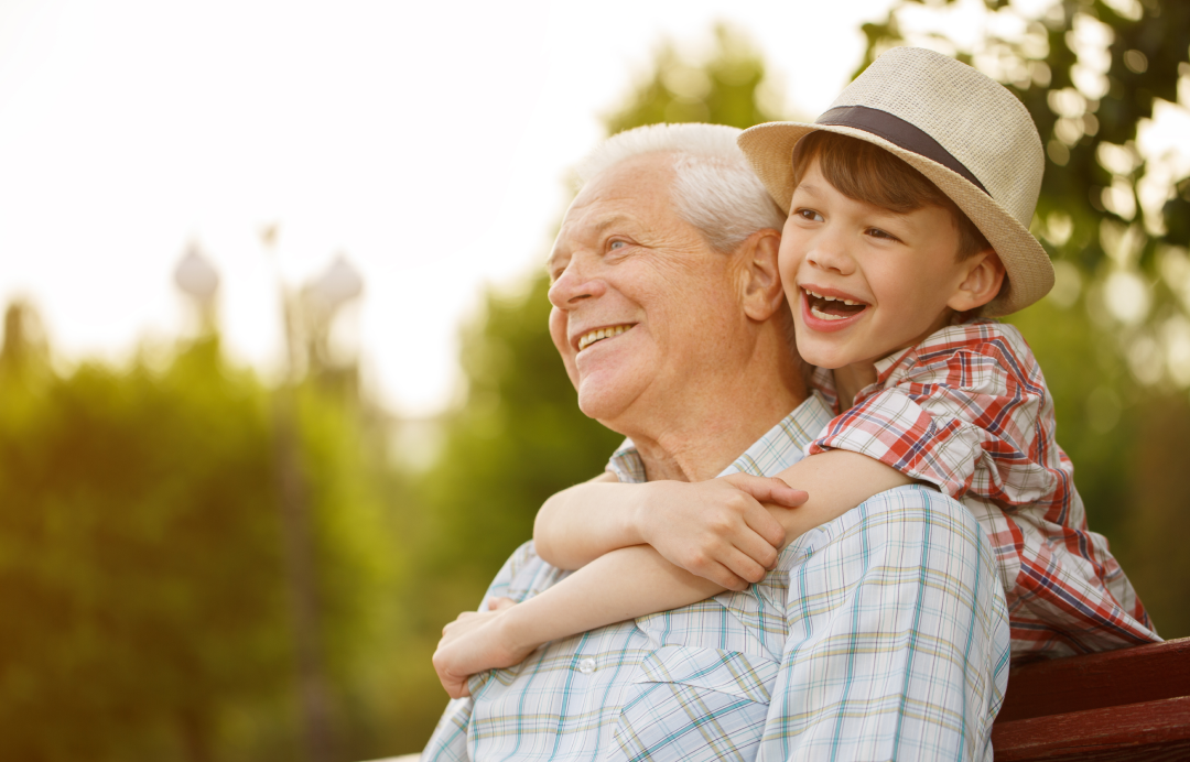 Child hugging smiling elderly man outdoors repsenting family care