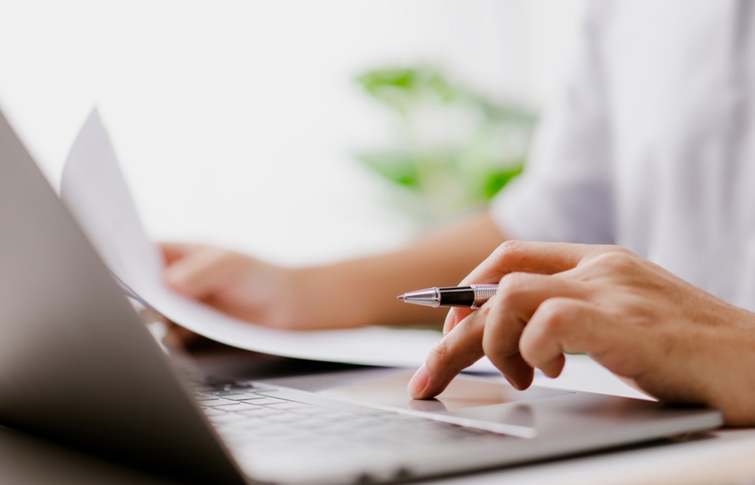 a person holding documents and working on a computer 