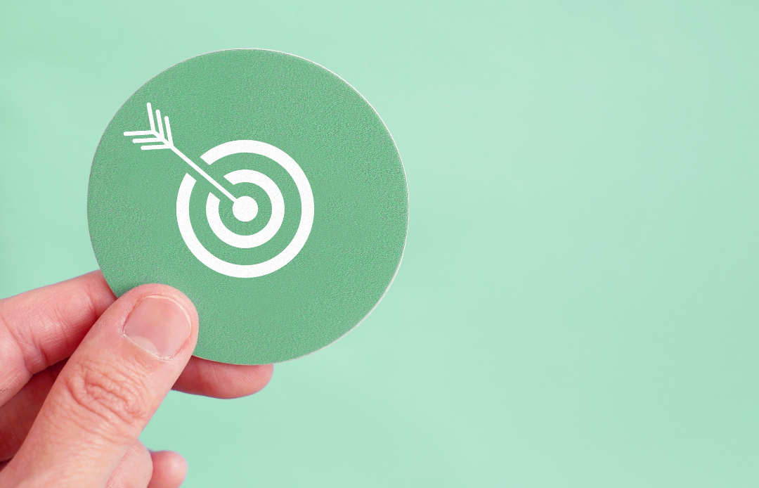 A hand holding a thin card with an arrow icon hitting a target on its fingertip