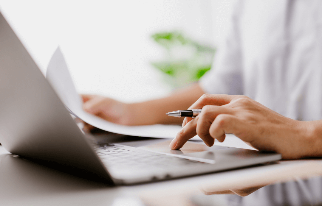 önünde laptop ve resmi belgeler bulunan kişi