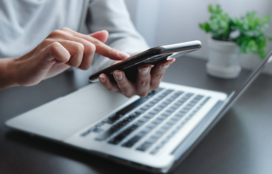bilgisayarı başında elindeki telefonla işlem yapan kişi