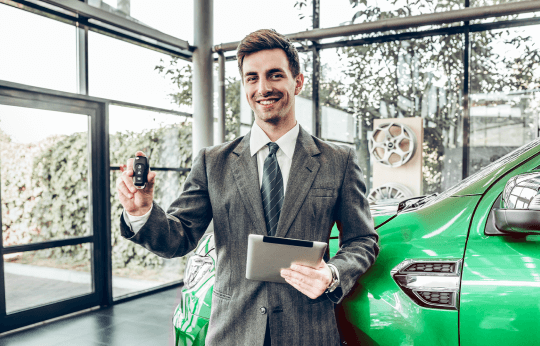 A sales consultant holding a car key and the concept of vehicle financing with a new vehicle