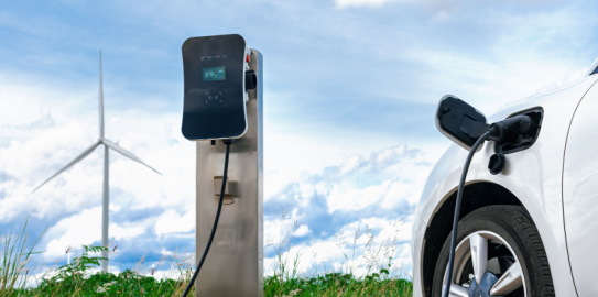 kablosu elektrikli araca bağlı Elektrikli araç şarj ünitesi ve arkasında rüzgar gülü