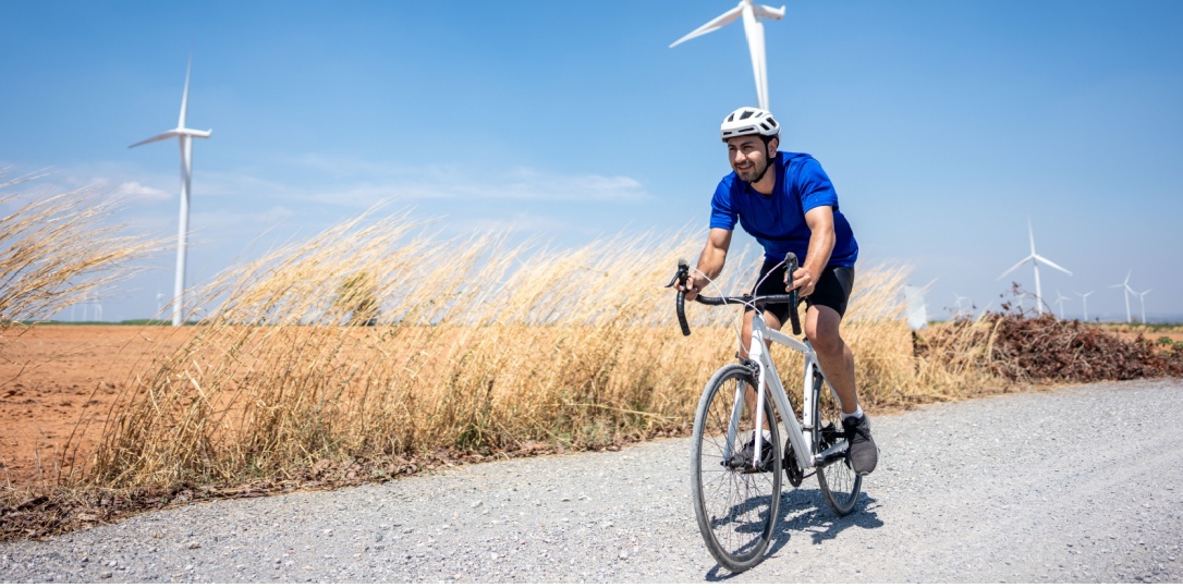 Rüzgar güllerinin olduğu arsa kenarında bisiklet süren kasklı genç