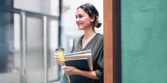 Üniversitede elinde kahvesi ve kitaplarıyla gülümseyen genç