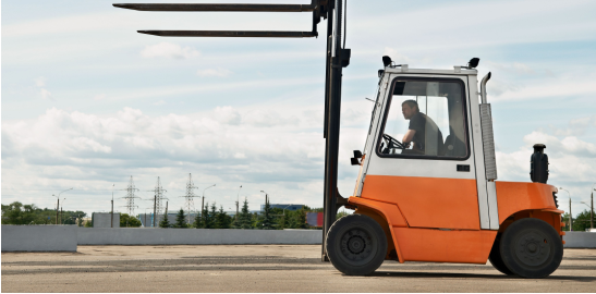 Açık alanda yük kaldıran turuncu forklift ve operatör