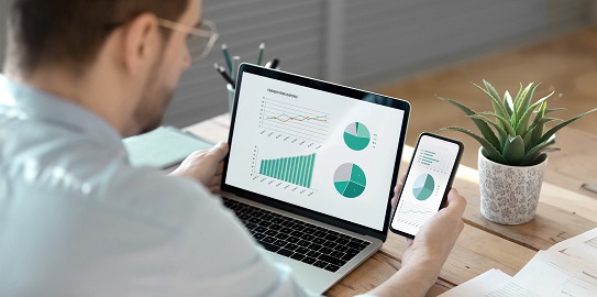 a businessman examining financial charts on his phone and computer screen