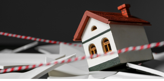 model house tilred among debris with caution tape symbolizing property damage