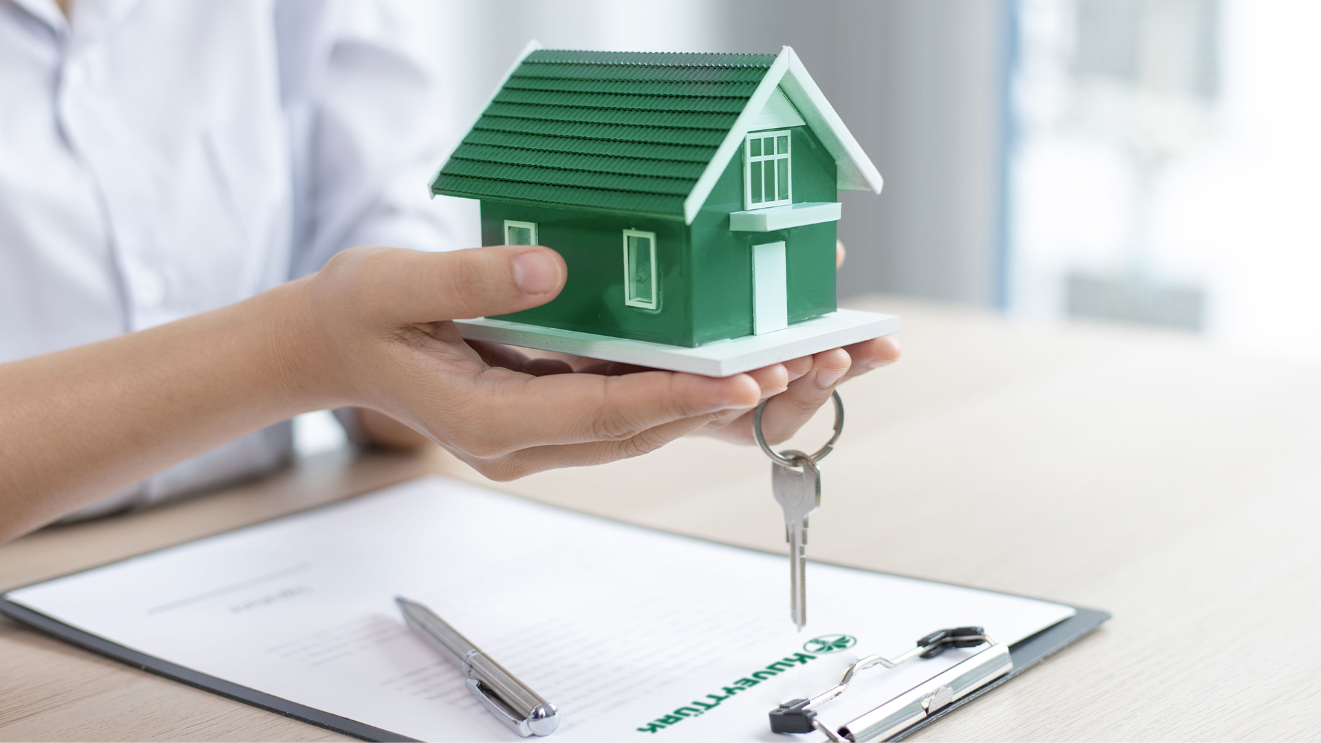 A model house and keys in hand along with a housing finance contract for home ownership