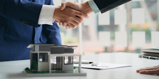 Two businessmen in suits shaking hands in an office setting