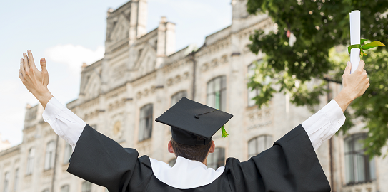 A young person in front of a university building with their arms outstretched wearing a graduation cap and gown and a young man in a gown holding his diploma