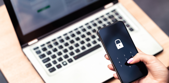 Person holding smartphone with lock screen near laptop