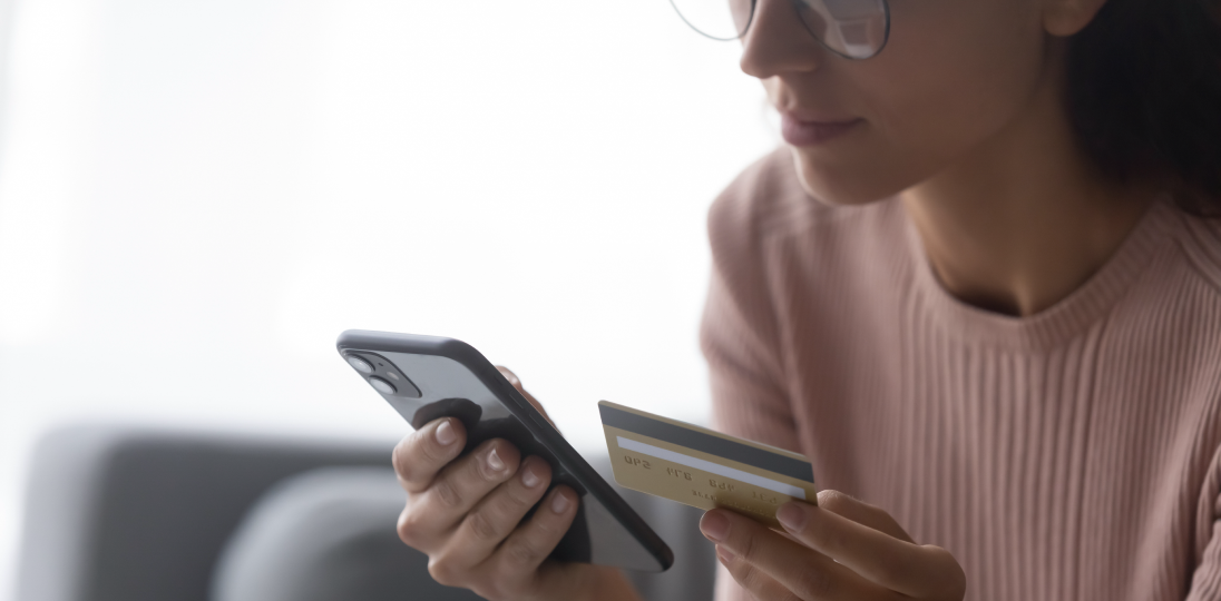 A young woman holding a phone in one hand and a credit card in the other