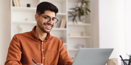 The bespectacled man smiling as he looks at the computer in front of him