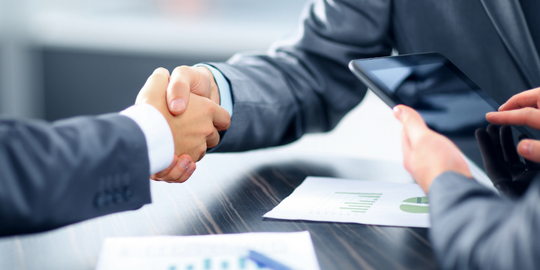 Two people shaking hands across a meeting table 