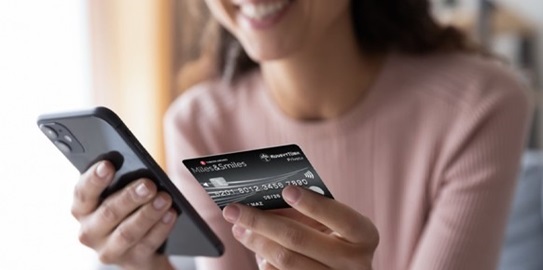 kredi kartına bakarak telefonundan hesap yapan kadın