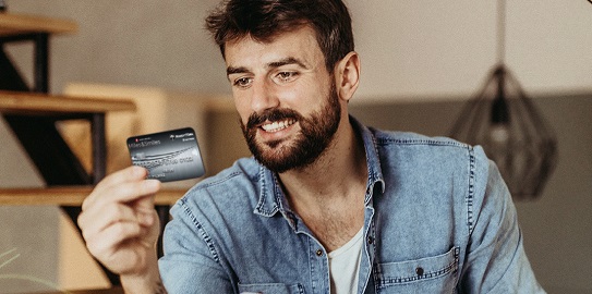 Ev ortamında oturan bir kişi kredi kartını inceliyor.