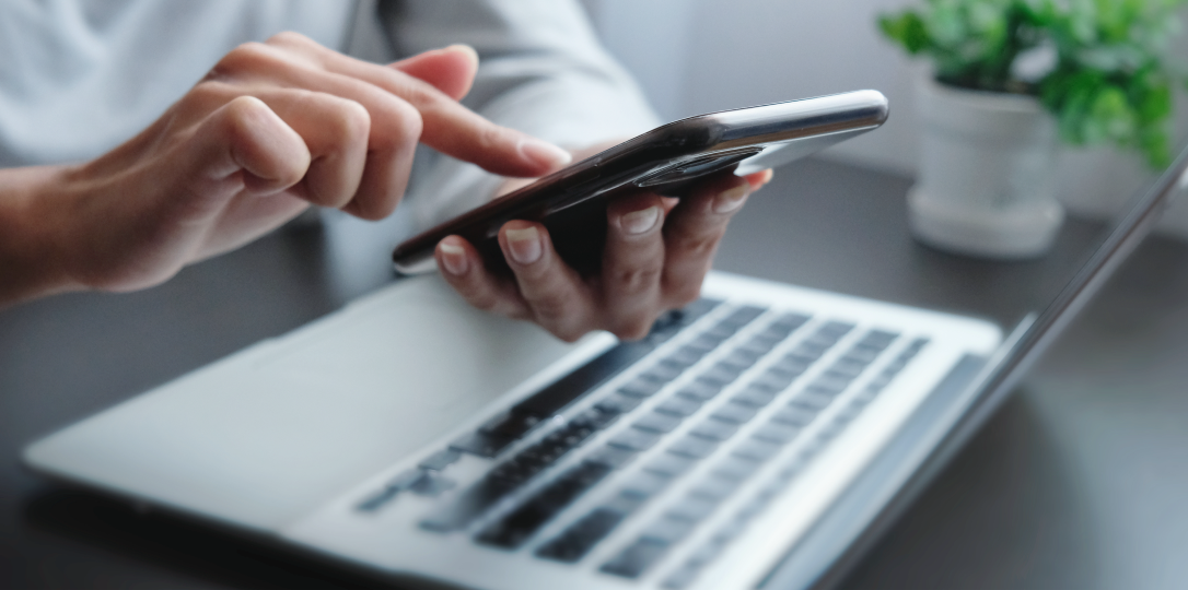 bilgisayarı başında elindeki telefonla işlem yapan kişi