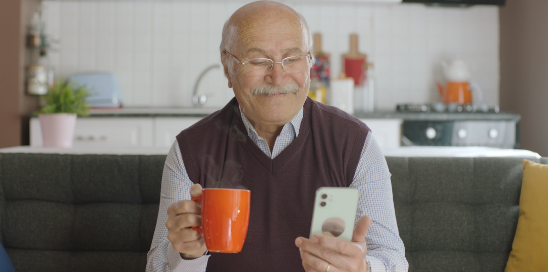 elinde kahvesi ile cep telefonuna bakan emekli adam
