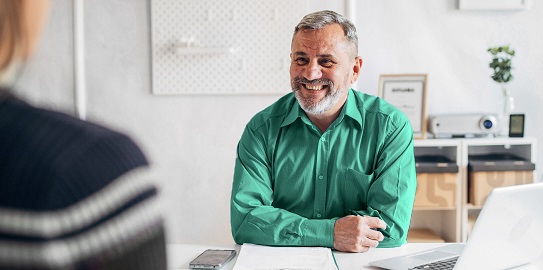 Ofis ortamında oturan ve gülümseyen orta yaşlı adam