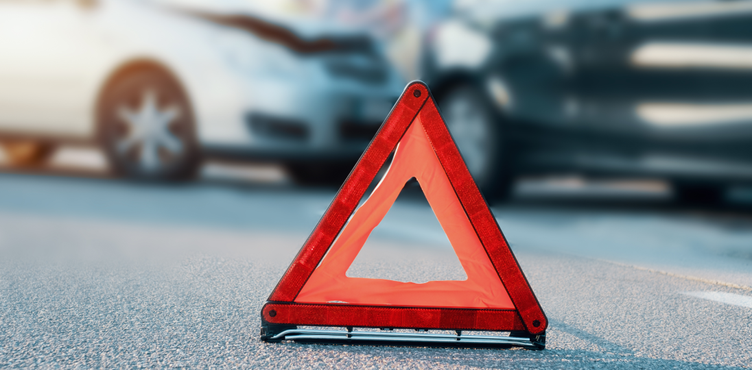 red warning triangle on road with blurred car accident in background