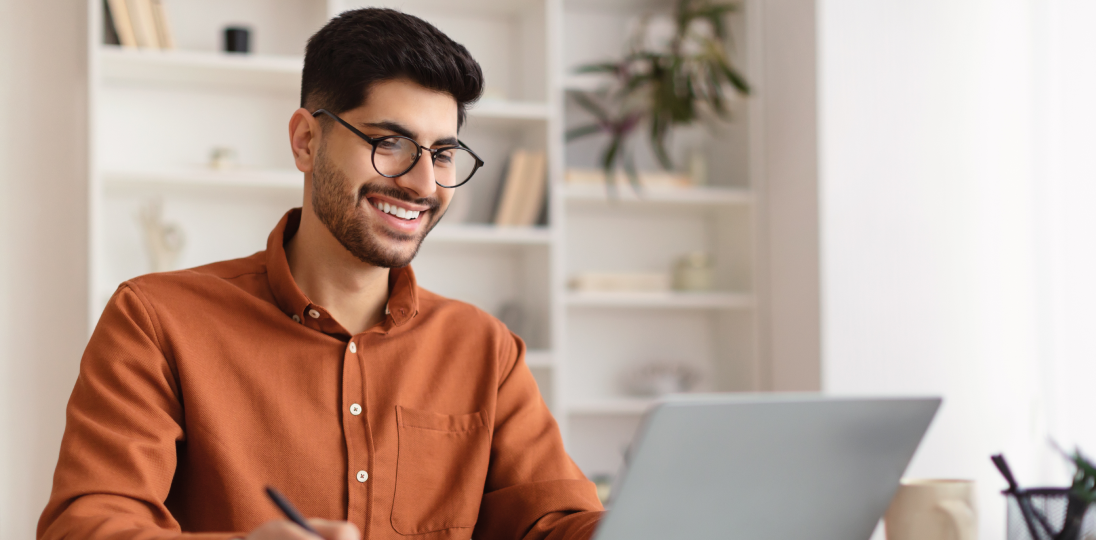 The bespectacled man smiling as he looks at the computer in front of him